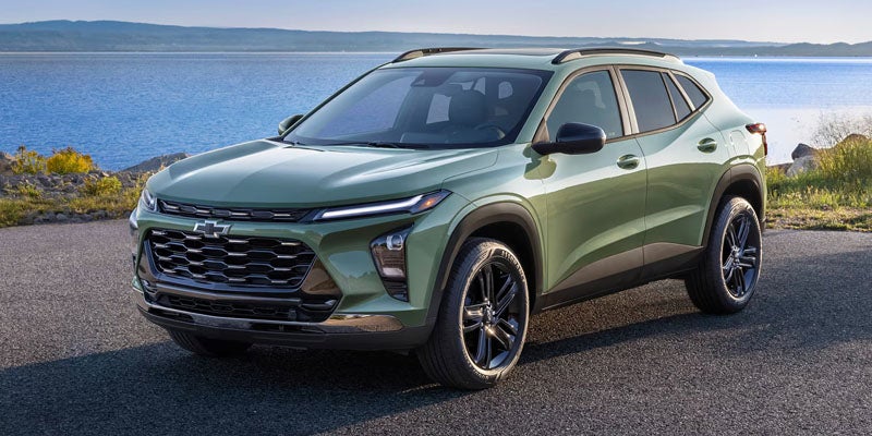 A shining moss-green 2026 Chevrolet Trax is parked in a lakeside parking area.